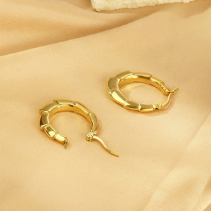 Détail des boucles d'oreilles en bambou doré sur un tissu en satin jaune clair
