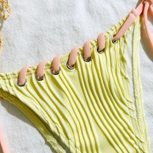 Detail of ribbed yellow bikini bottom featuring pink side ties and metal eyelets