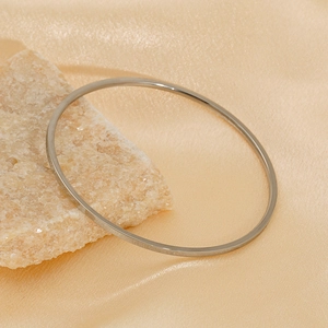 Minimalist silver stainless steel round bangle displayed on beige stone with silk background