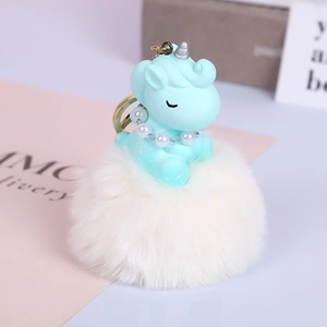 Close-up of blue plush unicorn with pearl necklace on white faux fur pompom keychain