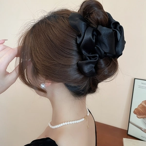 Detail of elegant black pleated satin oversized cloud scrunchie on a bun hairstyle