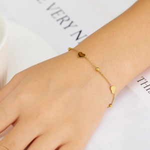 Detail of gold heart charm bracelet with zircons on wrist for bohemian styling
