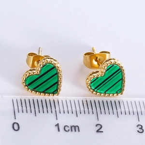 Macro shot of gold-plated heart earrings with green inlay next to a measuring ruler