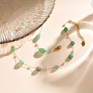 Detail of beaded necklace with green stones, white pearls, and gold K18 metal tag