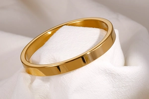 Detailed close-up of a polished gold stainless steel bangle on white fabric backdrop