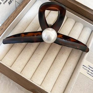 Detail of tortoise shell hair claw clip with large white pearl on a velvet jewelry box