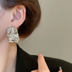 Close-up of silver irregular pleated square stud earring worn by a model in black suit