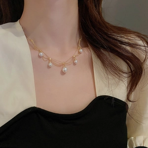Detail of layered gold-plated necklace with white faux pearls on model's neckline