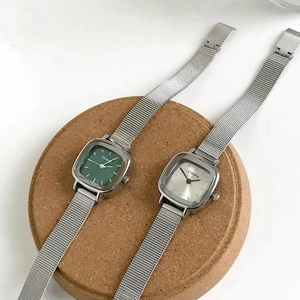 Flat lay of square green and white dial watches with silver mesh straps on cork