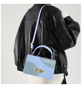 Detail of blue faux crocodile texture bag with stylish wave-shaped gold metal buckle