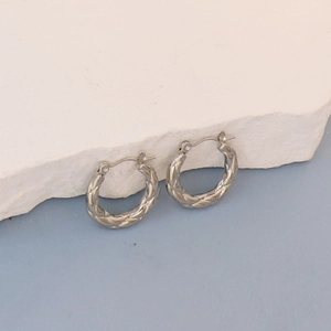 Detail view of silver oval hoop earrings with woven texture on a white stone display