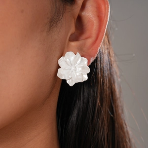 Gros plan d'une boucle d'oreille fleur blanche nacrée avec pétales superposés sur un mannequin