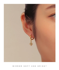 Close-up of golden starburst earrings with light blue zircon on a model ear