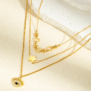 Détail d'un collier doré multicouche avec pendentifs œil protecteur, étoiles et cœurs sur pierre