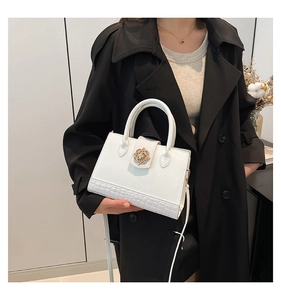 Close-up of white tote bag with crocodile texture and gold flower buckle on black coat