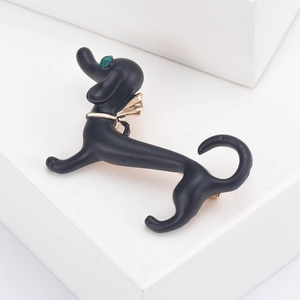 Close-up of matte black dachshund brooch with golden bow and green rhinestone eye detail