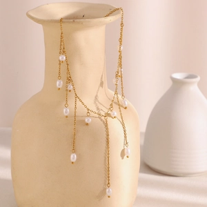 Collier à franges en acier doré 18K avec perles blanches sur un vase en céramique