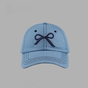 Detail of light blue denim baseball cap featuring dark blue bow embroidery and texture