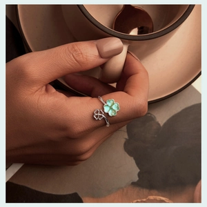 Close-up of green clover open ring on model hand holding coffee cup in warm light