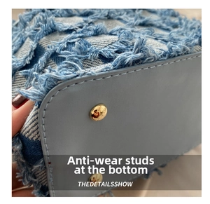 Close-up of denim shoulder bag bottom featuring golden metal studs and raw edge texture