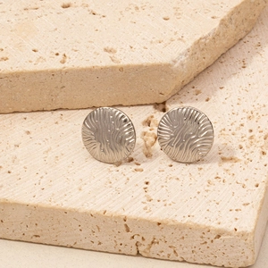 Macro detail of silver geometric ripple textured earrings on a beige stone surface