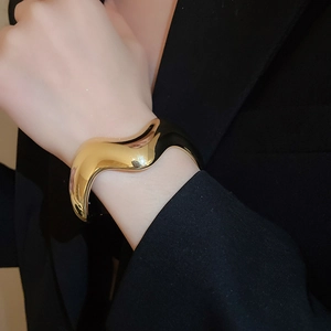 Dettaglio di un ampio bracciale a polsino ondulato in oro lucido indossato su una giacca nera