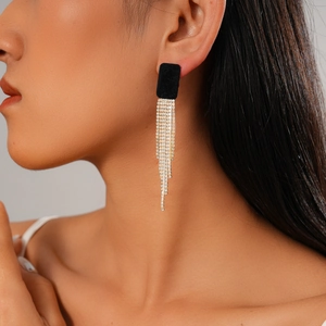Détail de boucles d'oreilles carrées en velours noir avec de longs pompons dorés en strass