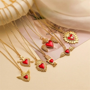 Collane dorate con pendenti a forma di cuore e ali in smalto rosso su superficie beige