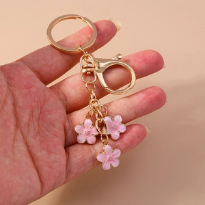 Close-up of hand-held gold keychain with three pink cherry blossom charms and petals