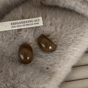 Detailed close-up of dark brown glazed pebble earrings on a soft plush beige background