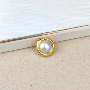 Close-up of a white round pearl earring with elegant gold plated metal border