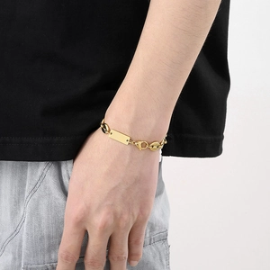 Detail of a gold pig nose chain bracelet with a polished rectangular tag on a man's wrist