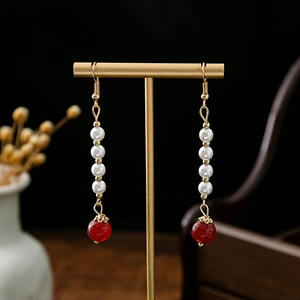Detail of long drop earrings with white pearls and red agate bead on a gold stand