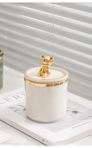 White ceramic jar with gold lid and bear handle placed on a minimalist magazine
