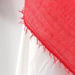 Detailed macro view of the frayed tassel edges on a red crinkled cotton linen scarf