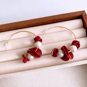 Detail of gold hoop earrings with red resin petals and white imitation pearls on velvet