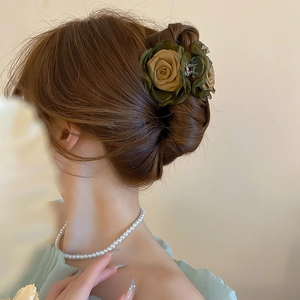Close-up of olive green and tan fabric rose hair claw clip worn by model in a bun