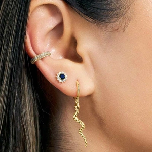 Close-up of gold ear cuff, blue gemstone flower stud, and snake dangle earring on model