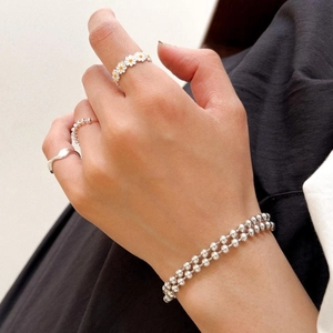 Detail of layered 925 sterling silver daisy ring and beaded bracelets on hand
