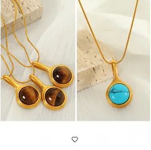 Detail of round tiger eye and turquoise pendants on gold snake chains over stone background