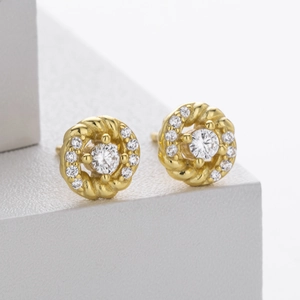 Detailed close-up of golden twist earrings with micro-set zircon on white stone