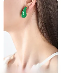 Close-up of a model wearing green teardrop earrings with a glossy enamel finish
