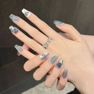 Nahaufnahme von Cat-Eye Kunstnägeln mit blauen Herzsteinen und grauem Metallic-Finish