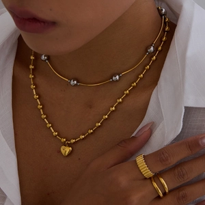 Gros plan d'un collier pendentif cœur doré et de bagues texturées sur un mannequin