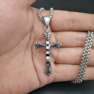 Macro shot of vintage stainless steel cross pendant with textured leaf patterns in hand