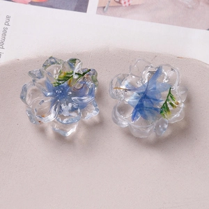 Macro detail of transparent resin earrings with blue dried flowers and green leaves