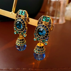 Macro detail of vintage gold clip-on earrings with blue crystals and green gemstone