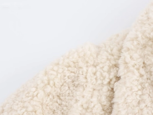 Detailed macro view of curly faux fur texture on a minimalist beige fleece coat fabric