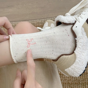 Detail of cream rib-knit mid-tube socks featuring colorful specks and pink bow embroidery