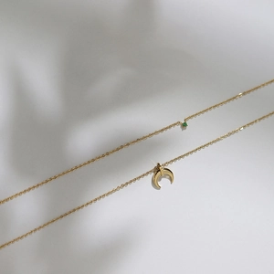 Detailed view of a gold double-layer necklace with crescent moon and green gemstone